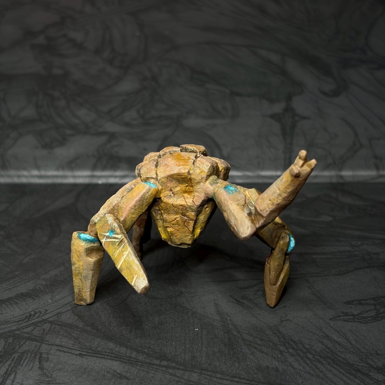 May include: A detailed sculpture of a stylized insectoid creature. The figure is primarily brown with gold accents and turquoise details. The creature has multiple legs and a segmented body, with its arms raised.