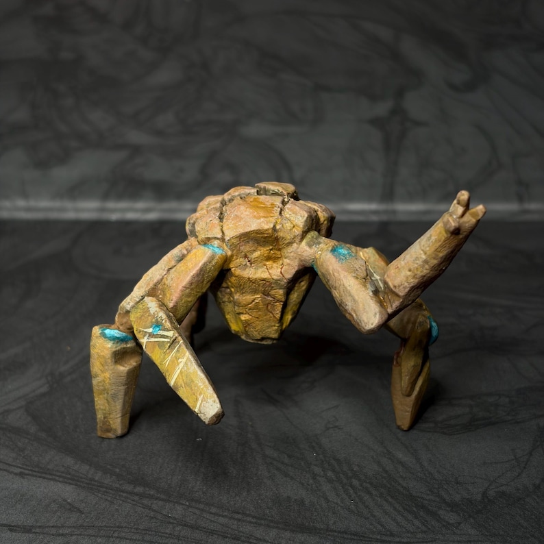 May include: A handcrafted, stylized sculpture of a creature with a segmented body and legs. The sculpture is primarily brown with gold accents and small blue details. The creature's pose suggests movement, with one arm raised.