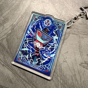 May include: A rectangular acrylic keychain featuring a cartoon character with a screen-shaped head, red eyes, and a sharp-toothed grin. The design is set against a blue background with white lightning-like patterns and a decorative border. A silver chain and clasp are attached.