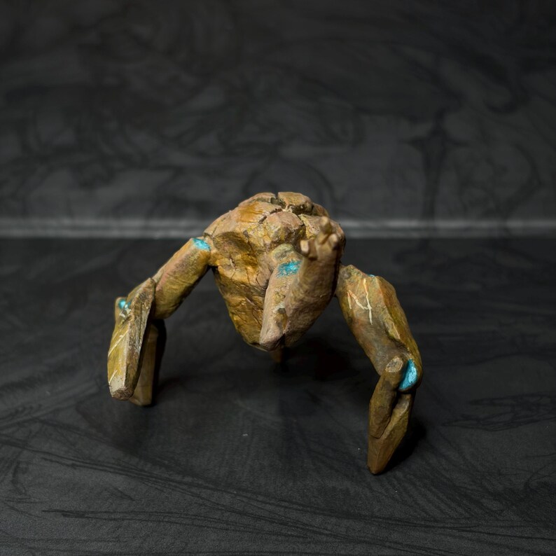 May include: A handcrafted, abstract sculpture of a creature with a rough, textured surface. The sculpture is primarily brown with accents of teal blue. The figure has a body and two pairs of limbs, giving it a unique, artistic appearance.