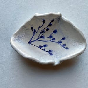 May include: A white ceramic dish with an irregular shape and a blue floral design. The dish is perfect for holding small items like jewelry or keys.