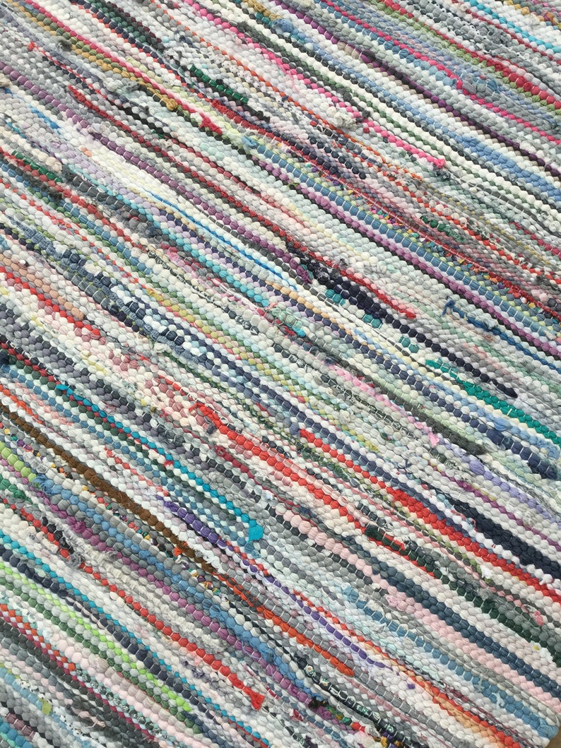 Pu&ograve; includere: Un tappeto multicolore tessuto con un motivo a righe. Il tappeto presenta una miscela di colori tra cui rosso, blu, verde e grigio. Il tappeto &egrave; realizzato con strisce di tessuto e ha un aspetto strutturato. Le strisce corrono in diagonale.