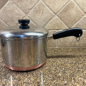 May include: A set of three ceramic nesting bowls in graduating sizes. The bowls feature a speckled, cream-colored exterior and a contrasting dark brown interior. The largest bowl measures approximately 8 inches in diameter.