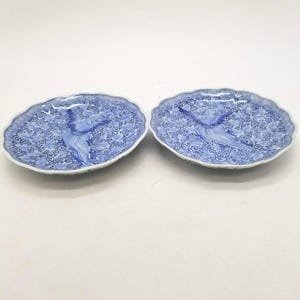 May include: Two blue and white ceramic oval plates with a scalloped edge. Each plate features a central bird design and a swirling pattern. The plates are likely for decorative or serving purposes.