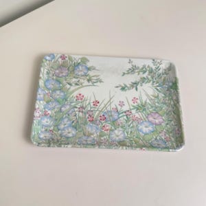 May include: A rectangular serving tray featuring a botanical illustration of blue morning glory flowers, small pink blossoms, and green foliage scattered across a white background. The tray has rounded corners and a smooth, flat surface design.
