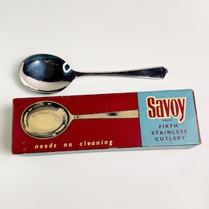 May include: A shiny, stainless steel spoon with a rounded bowl and a slender handle. The spoon is next to a red and blue box with the text "Savoy Brand Firth Stainless Cutlery" and "needs no cleaning."