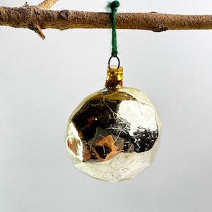 May include: A vintage Christmas bauble with a textured, silver and gold finish. The round bauble is suspended from a brown branch with a green string. The bauble has a reflective surface.