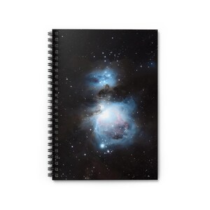 Op de afbeelding: Spiraalgebonden notitieboek met een opvallende afbeelding van een nevel. De omslag toont een kleurrijke kosmische scène met blauwe, roze en witte tinten tegen een donkere, met sterren bezaaide achtergrond. Het notitieboek heeft een witte achtergrond.