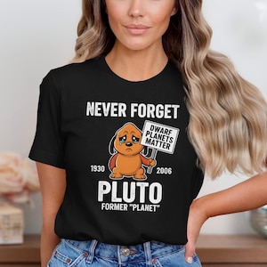 May include: Black t-shirt with the text "NEVER FORGET" and a cartoon Pluto graphic. The graphic includes the text "DWARF PLANETS MATTER" and the years 1930 and 2006. The shirt also says "PLUTO FORMER 'PLANET'".