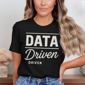 May include: Black t-shirt with the words "DATA Driven" printed in white. The word "DATA" is in a bold, sans-serif font, while "Driven" is in a cursive font. The word "DRIVEN" is also printed below in a smaller font.