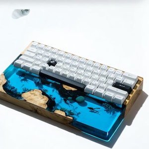 May include: A custom mechanical keyboard with white keycaps and a unique design. The keyboard features a wooden base with a clear blue resin inlay depicting an underwater scene with coral and fish. The keyboard measures approximately 12 inches long.