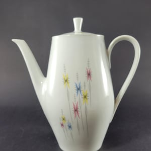 May include: White ceramic coffee pot with a lid and handle. The pot is decorated with colorful floral designs in yellow, pink, and blue. The spout is long and slender, and the handle is curved.