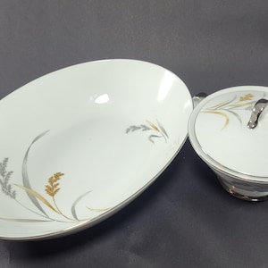 May include: A white porcelain serving bowl and a covered dish with a silver trim and a delicate floral design in shades of grey and gold.