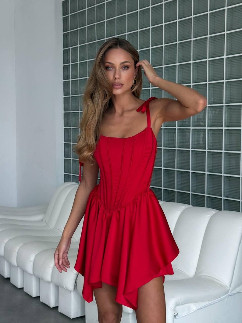 Puede incluir: Un vestido rojo vibrante con un corpi&ntilde;o ajustado y una falda acampanada. El vestido presenta delicadas correas anudadas y una silueta favorecedora. La tela parece tener un ligero brillo, lo que aumenta su atractivo elegante. Una opci&oacute;n elegante para ocasiones especiales.
