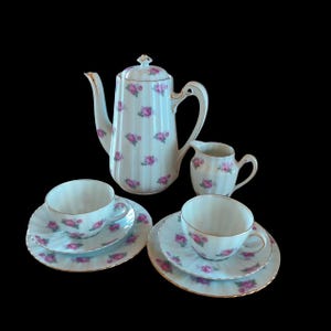 Può includere: Servizio da tè in porcellana vintage con sfondo bianco e motivo a rose rosa. Il set comprende una caffettiera, una lattiera, due tazze e piattini. I bordi sono rifiniti con dettagli dorati. Ideale per servire tè o caffè.