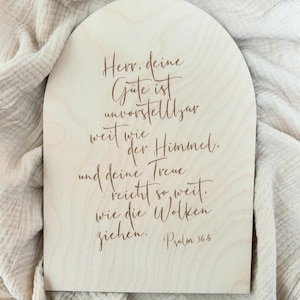 Könnte beinhalten: Ein Holzschild mit abgerundeter Oberseite, auf dem ein Zitat in deutscher Sprache über Gottes Güte und Treue steht. Das Zitat lautet: "Herr, deine Güte ist unvorstellbar weit wie der Himmel. und deine Treue reicht so weit. wie die Wolken ziehen." Psalm 36:6