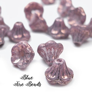 May include: A scattering of iridescent pink glass beads with a flower-like design. The beads have a textured surface and a metallic sheen.  Blue Fire Beads.