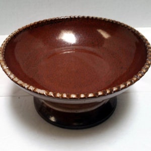 May include: A brown ceramic bowl with a white rim and a scalloped edge. The bowl has a pedestal base.