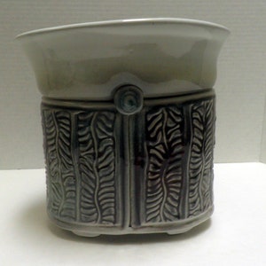 May include: A white ceramic planter with a gray and purple design. The planter has a wide rim and a rounded base.