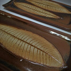 May include: Two rectangular ceramic serving trays with a brown glaze and a leaf design. The leaves are embossed and have a light brown color.
