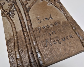 May include: A ceramic wall hanging with a textured brown background and a relief sculpture of trees. The text "Find peace in nature" is inscribed on the wall hanging.
