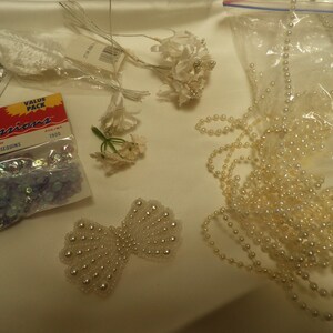 May include: A package of 5mm cupped sequins in a light blue color. The package is labeled "Crafting Expressions" and "Value Pack". There is also a white pearl garland and white floral embellishments.
