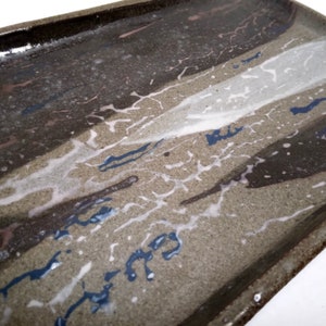 May include: A rectangular ceramic serving tray with a brown, white, and blue glaze. The glaze has a mottled, abstract pattern.