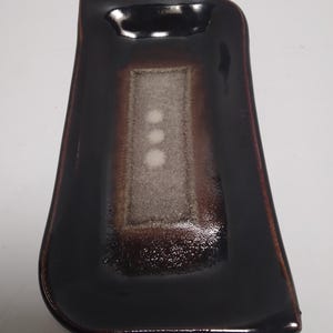 May include: A rectangular ceramic dish with a dark brown exterior and a lighter brown interior. The center features a rectangular design with three white dots. The dish has a glossy finish.