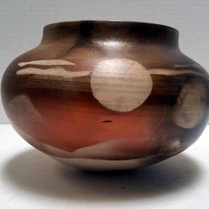 May include: A brown ceramic pot with white and brown abstract designs. The pot has a rounded shape and a wide opening.
