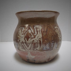 May include: A brown ceramic vase with a white and brown abstract design. The vase has a rounded body and a wide opening.