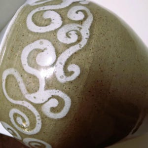 May include: A ceramic vase with a light brown glaze and white swirl design.