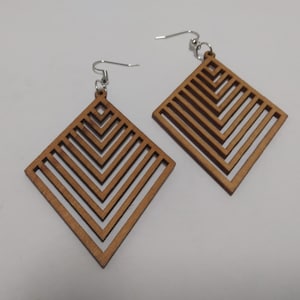 May include: A pair of wooden earrings with a geometric design. The earrings are shaped like diamonds and have a series of parallel lines that create a chevron pattern.
