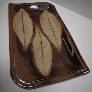 May include: A rectangular ceramic serving tray with a brown glaze and three raised leaf designs in a lighter brown color.