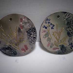 May include: Two round ceramic wall hangings with a white background and gold and blue floral designs. The hangings are labeled A and B.