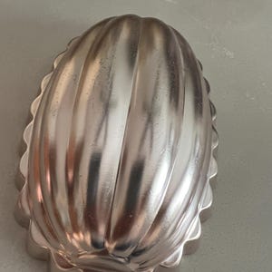 May include: A silver-colored metal mold shaped like a melon with a scalloped edge. The mold has a smooth, shiny surface and is designed for baking.