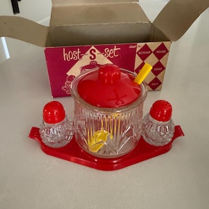 May include: A vintage red and clear glass host-s-set with a box. The set includes a lidded jar, two shakers, and a tray. The box is red and white with the words "host-s-set" printed on it.