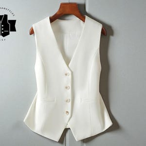 May include: A cream-coloured waistcoat with a V-neck and four buttons. The waistcoat has two front pockets and is hanging on a wooden hanger. The logo "CLASSYBIRANSTYLES VEST" is in the upper left corner.