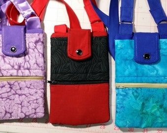 Puede incluir: Tres bolsas de teléfono de tela con compartimentos con cremallera y cierre de solapa. Las bolsas son de color morado, rojo y azul con diferentes patrones. Cada bolsa tiene una correa para llevar.