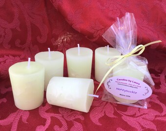 May include: Six small, white, unscented votive candles, with one candle packaged in a clear plastic bag tied with a yellow ribbon. The bag has a label that reads "Candles by Laura", "Hand poured - One of a kind", "www.stubos.etsy.com", "Honeysuckle", and "Maine USA".