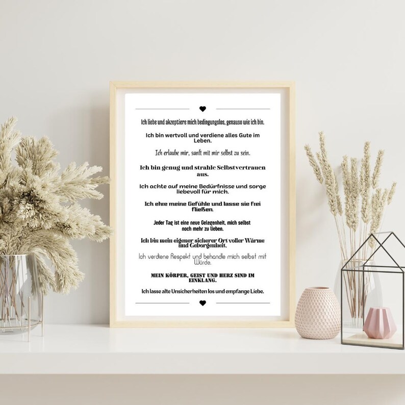 May include: A black and white printable poster with a motivational quote in German. The quote is about self-love and acceptance. The poster is framed and hanging on a white wall.