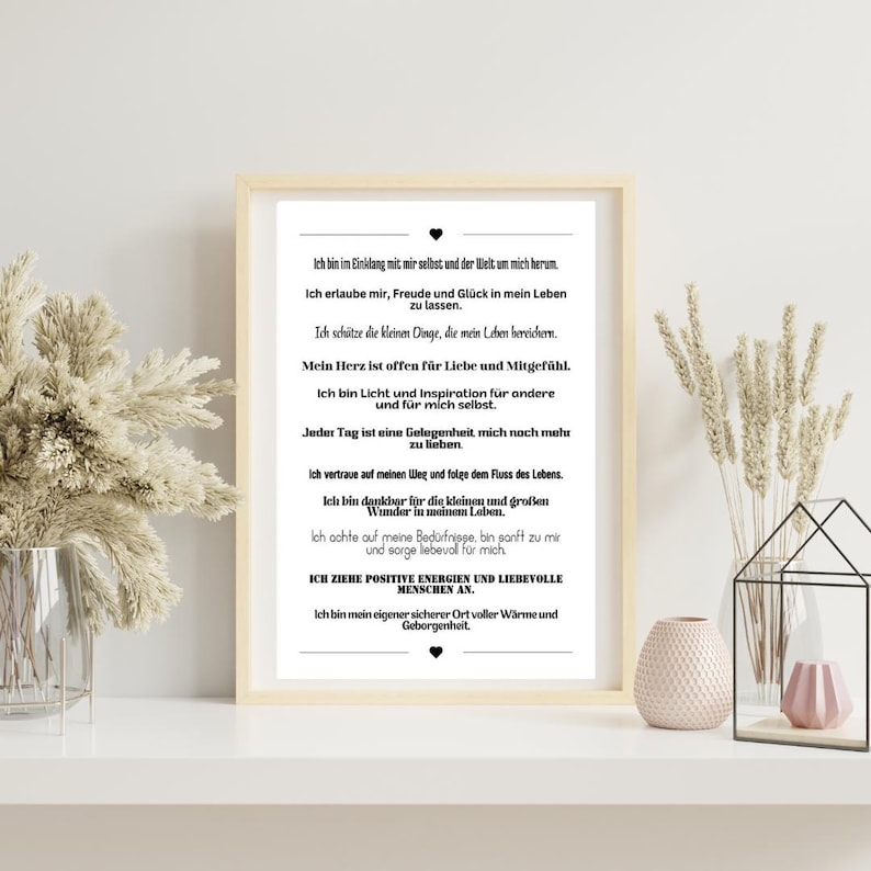 May include: A framed print with a cream-colored border, featuring black text in German. The text includes affirmations about self-love, gratitude, and positivity. The print is displayed on a white surface with decorative elements.