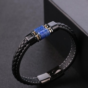 May include: Black braided leather bracelet with a blue stone centre and silver-tone clasp. The bracelet has a woven design and a magnetic clasp. The blue stone is a focal point, adding a pop of colour to the accessory.
