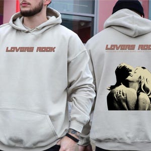 May include: Two beige hoodies with the text "Lovers Rock" printed on the front. One hoodie features a graphic of a couple embracing. The text below the graphic reads "Because love can burn like a cigarette."