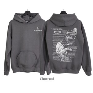 May include: Charcoal gray hoodie with a front pocket and hood. The front features a small cross design. The back displays a detailed graphic with the text "FORGIVE THEM FATHER" and a depiction of a crown of thorns and a figure.