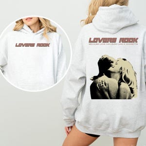 May include: A gray hoodie with the text "LOVERS ROCK" in brown on the front and a black and white image of a couple embracing with the text "BECAUSE LOVE CAN BURN LIKE A CIGARETTE" on the back.