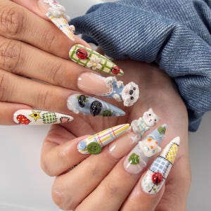 Pode incluir: Unhas postiças longas em formato stiletto com uma variedade de designs 3D, incluindo joaninhas, flores brancas, botões verdes e pequenas figuras de animais esculpidas. A nail art incorpora padrões xadrez, motivos patchwork e tons pastéis.