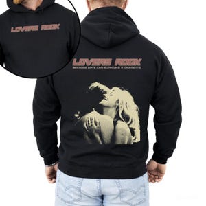 May include: Black hooded sweatshirt with a graphic print of a couple embracing. The text "LOVERS ROCK" is printed in a retro style font with the tagline "Because love can burn like a cigarette".