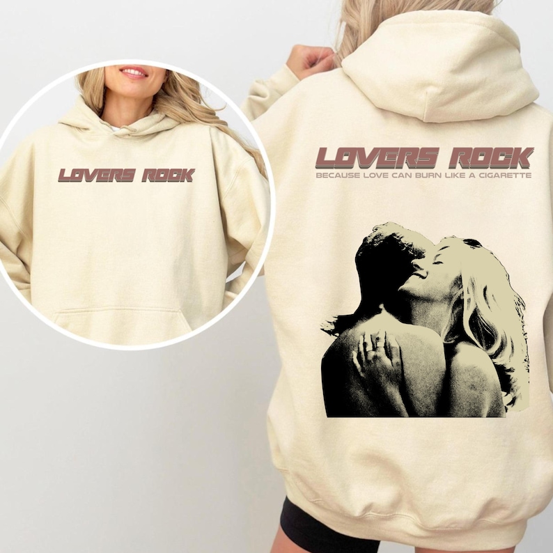 May include: A cream-colored hoodie with a graphic print of a couple embracing. The text "LOVERS ROCK" is printed in brown on the front of the hoodie, and the text "BECAUSE LOVE CAN BURN LIKE A CIGARETTE" is printed in brown below the graphic.