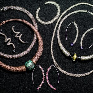May include: A set of silver and copper wire jewelry, including necklaces, earrings, and bracelets. The jewelry features a variety of designs, including a turquoise stone pendant.