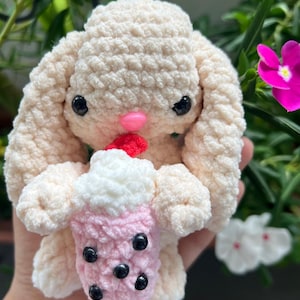 May include: A crocheted plush bunny holding a pink and white crocheted boba tea cup with black boba pearls.